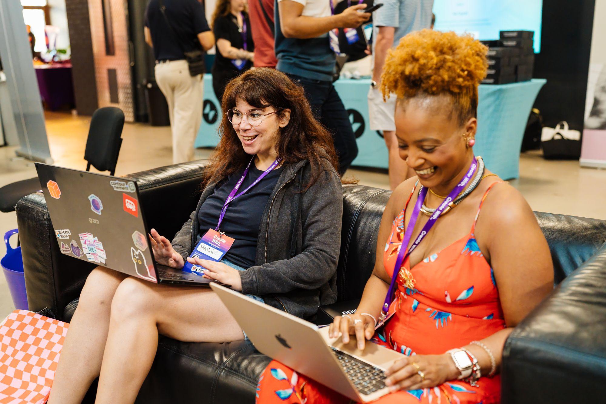 Two attendees building on their laptops on a sofa in the Creator Lounge