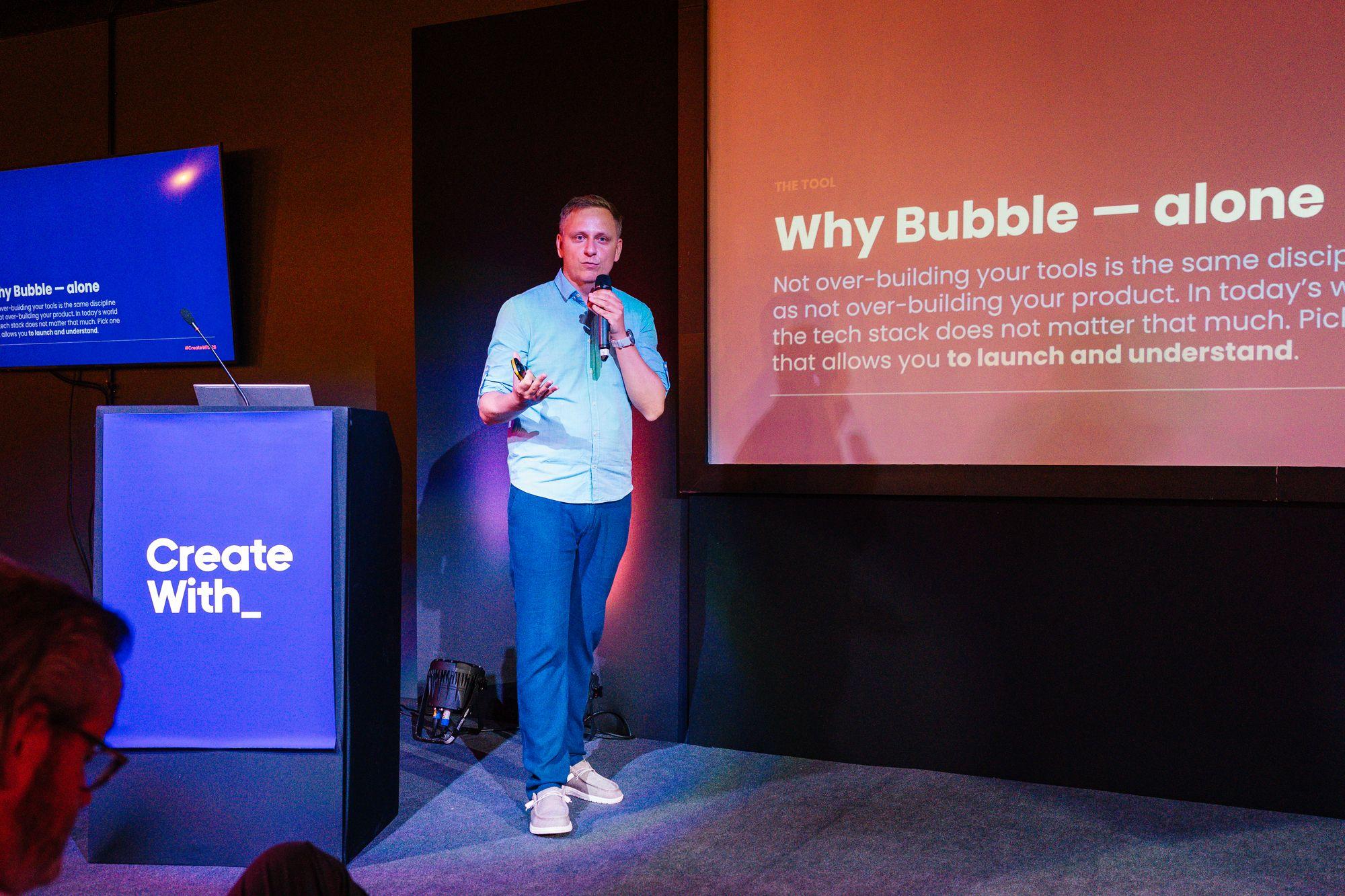 A speaker on stage in front of a Why Bubble slide
