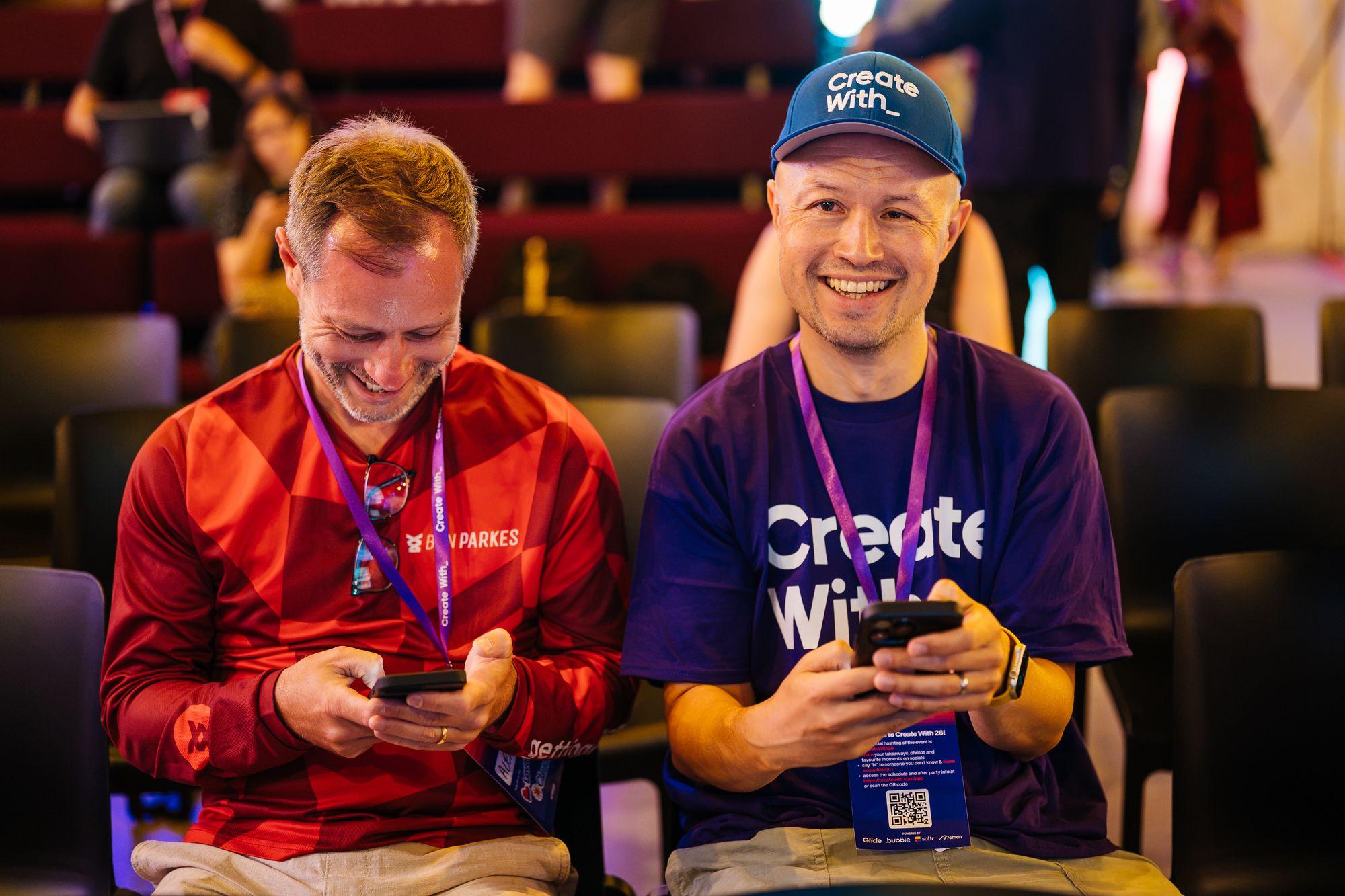 Two attendees in the audience smiling at their phones, one in a Create With cap