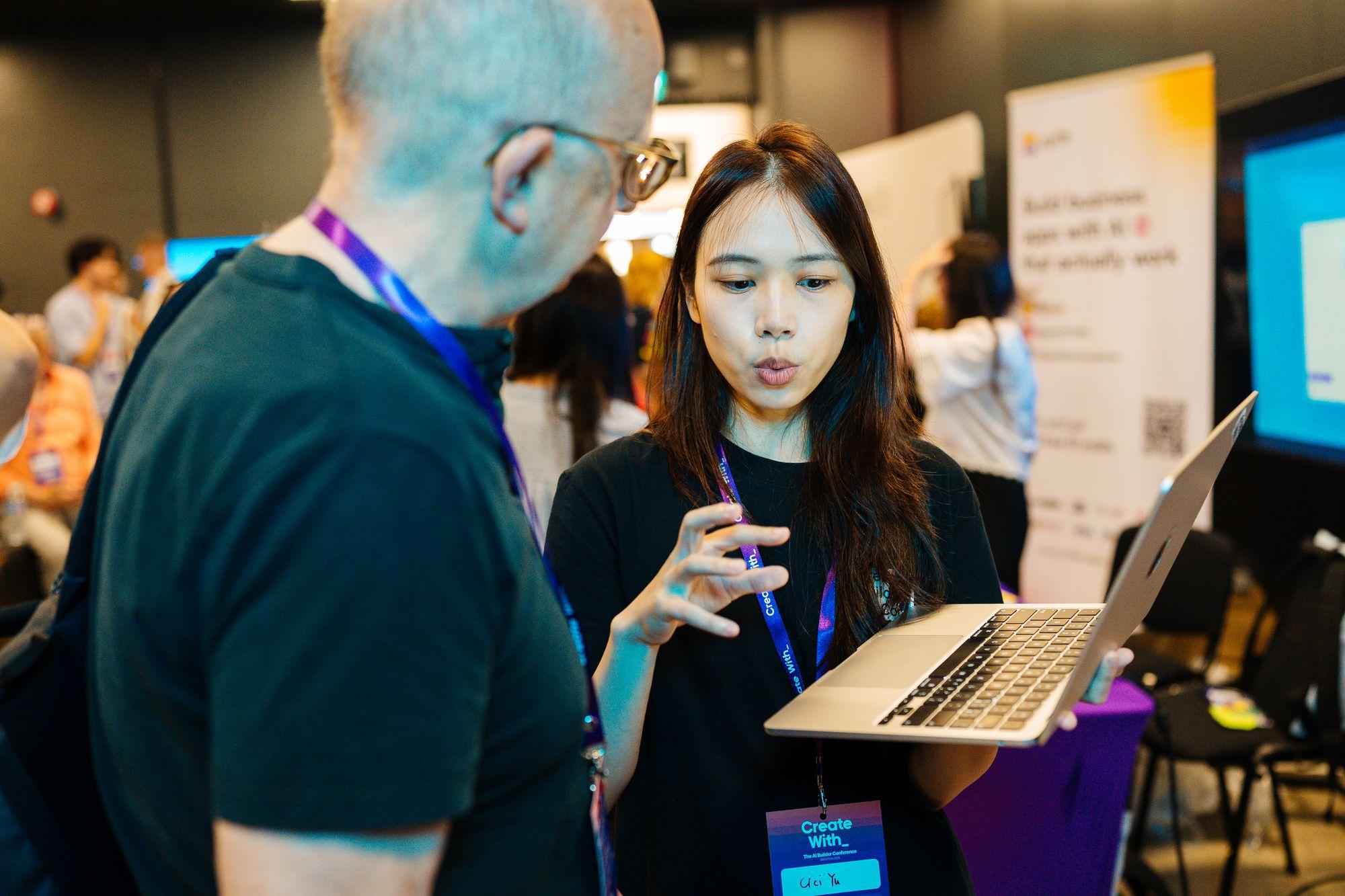 An attendee showing her laptop to another attendee at a stand