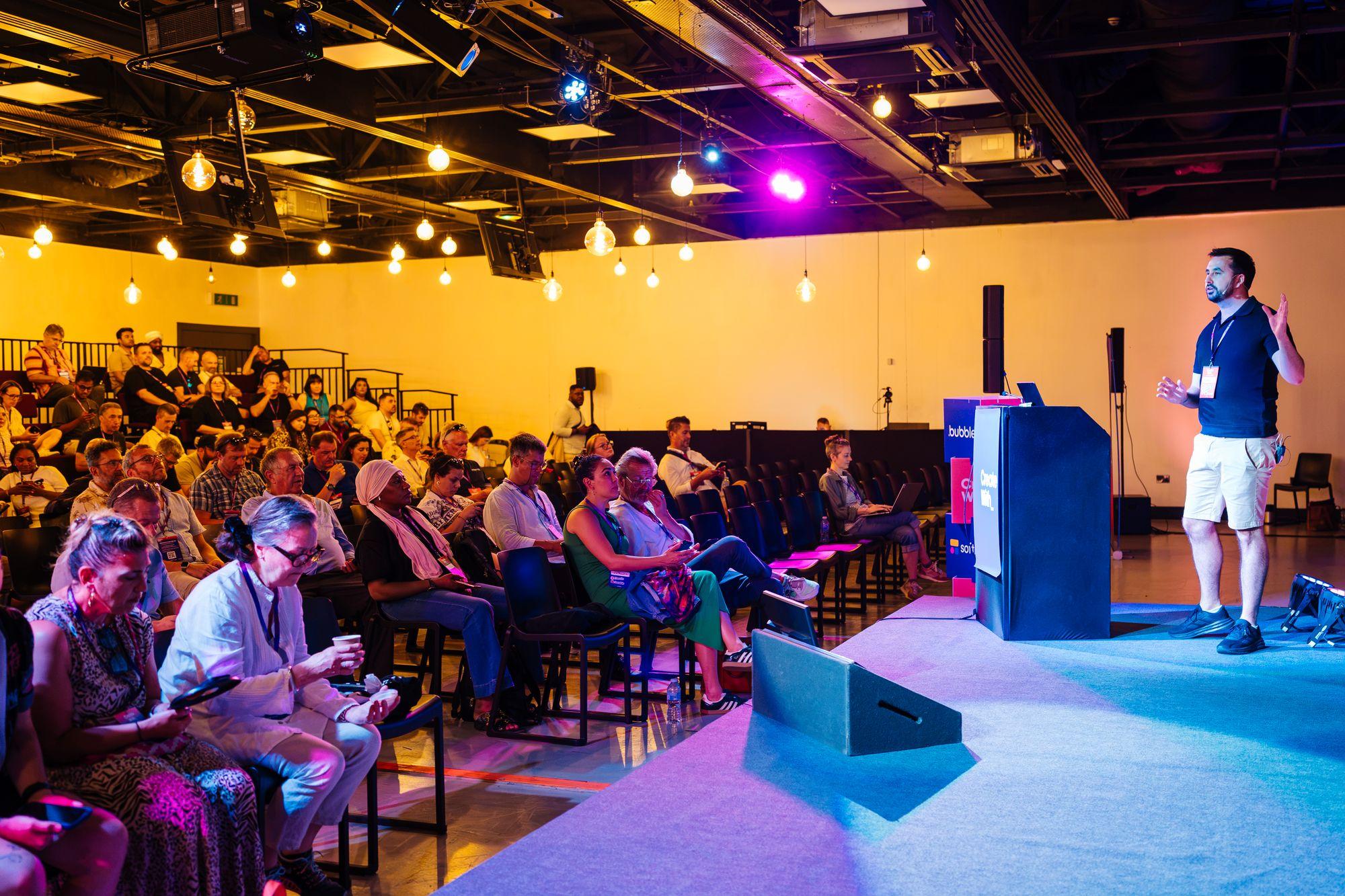 A speaker on stage in warm light with the audience seated