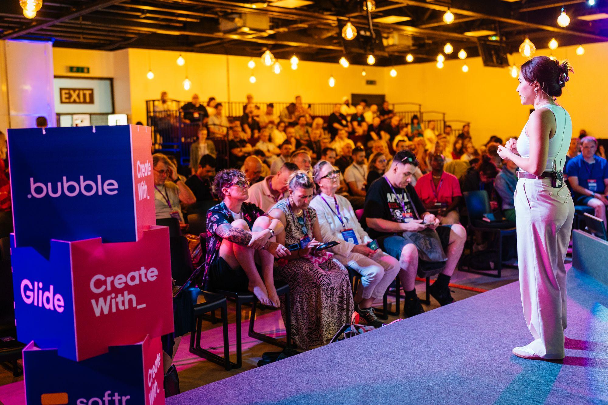A speaker seen from the audience, sponsor cubes at the front
